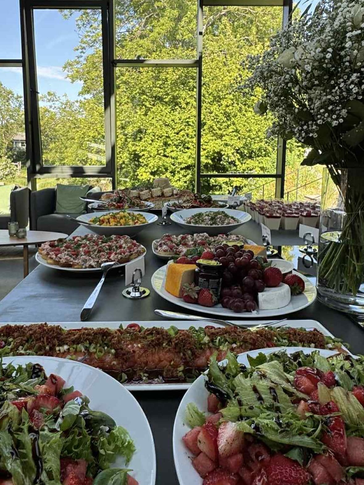 Oppdekket buffet med fat av tapas, salater og spekemat i et lokale med utsikt til hage